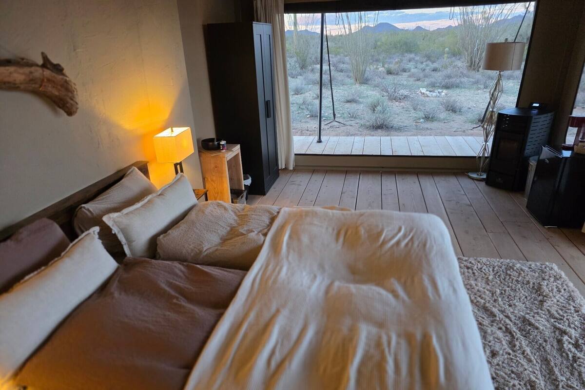 A bedroom with a large bed, a desk, a lamp, and a view of a desert landscape.