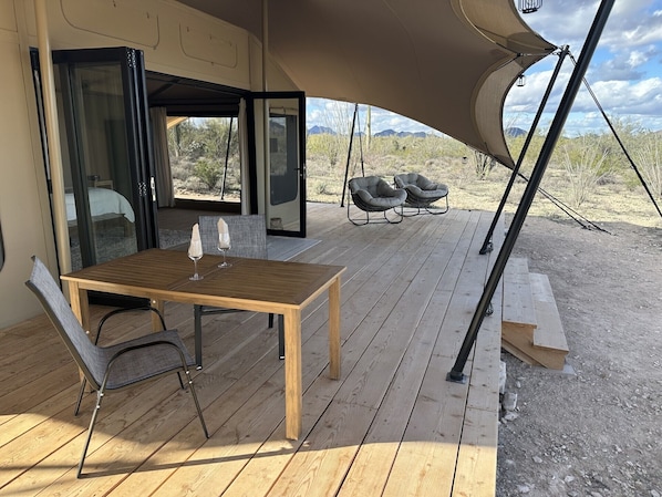 A wooden deck with a table and chairs, a covered area with a view of desert landscape. - SaguaroGlamp (Marana)