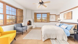 A bedroom with a bed, a desk, a chair, a fireplace, and large windows. - SaguaroGlamp (Marana)
