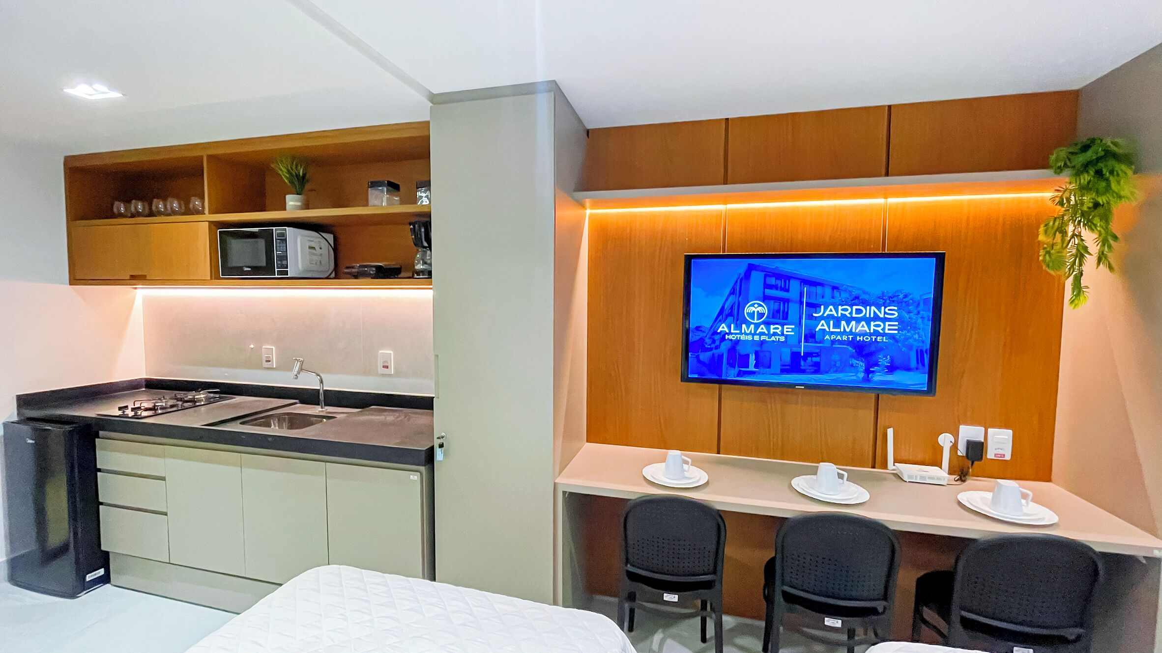 Una cocina moderna con microondas integrado, un lavamanos y una zona de comedor con un televisor mostrando el nombre del hotel.