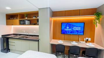 Una cocina moderna con microondas integrado, un lavamanos y una zona de comedor con un televisor mostrando el nombre del hotel.