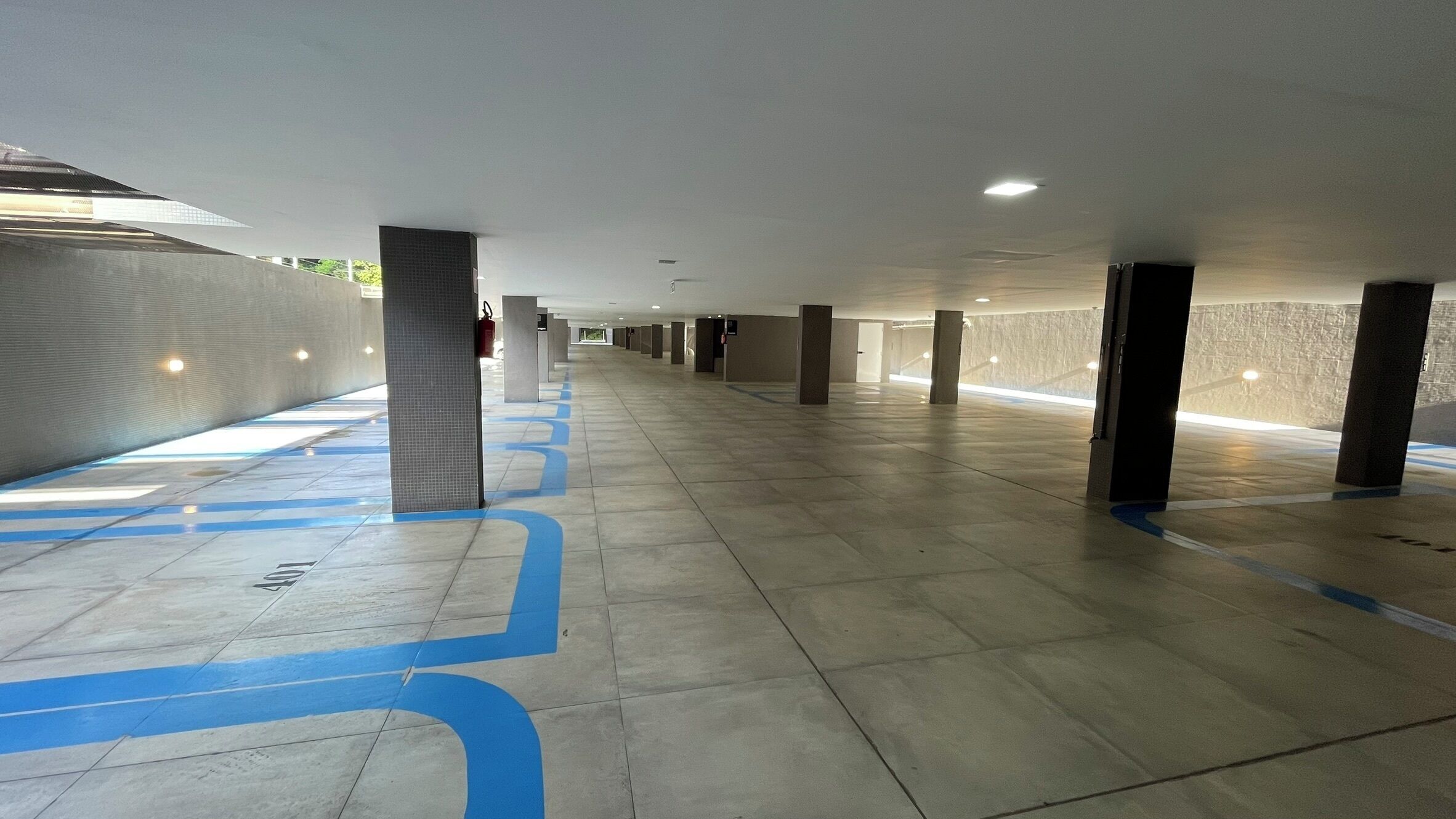 A spacious indoor corridor with tiled flooring and blue directional markings.