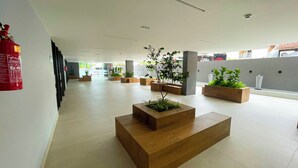 Un hall espacioso con extintor en la pared, varios maceteros de madera con plantas verdes y un diseño moderno y limpio.