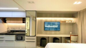 Habitación de hotel moderna con kitchenette, televisión de pantalla plana en la pared y cama con cubrecama blanco.