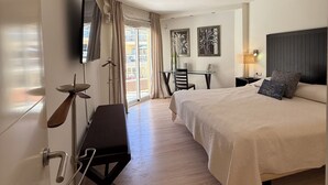 Habitación de hotel con cama, escritorio, silla, televisor montado en la pared y ventana con cortinas.