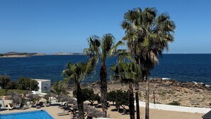 Un espace piscine doté de chaises longues et de parasols, offrant une vue sur une plage bordée de palmiers et un ciel d’un bleu limpide.