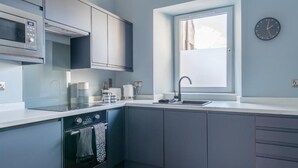 A modern kitchen with grey cabinets, a built-in oven, a microwave, and a window above the sink.