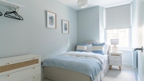 A bedroom with a bed, bedside tables, a dresser, and a window with blinds.