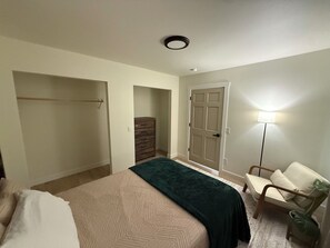 A bedroom with a bed, a dresser, a chair, a lamp, and a door. - Enchanting whole home on Nancy lake with WiFi in Willow Alaska! (Willow)