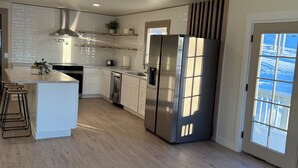 A modern kitchen with a central island, stainless steel appliances, and a view through a large window. - Enchanting whole home on Nancy lake with WiFi in Willow Alaska! (Willow)