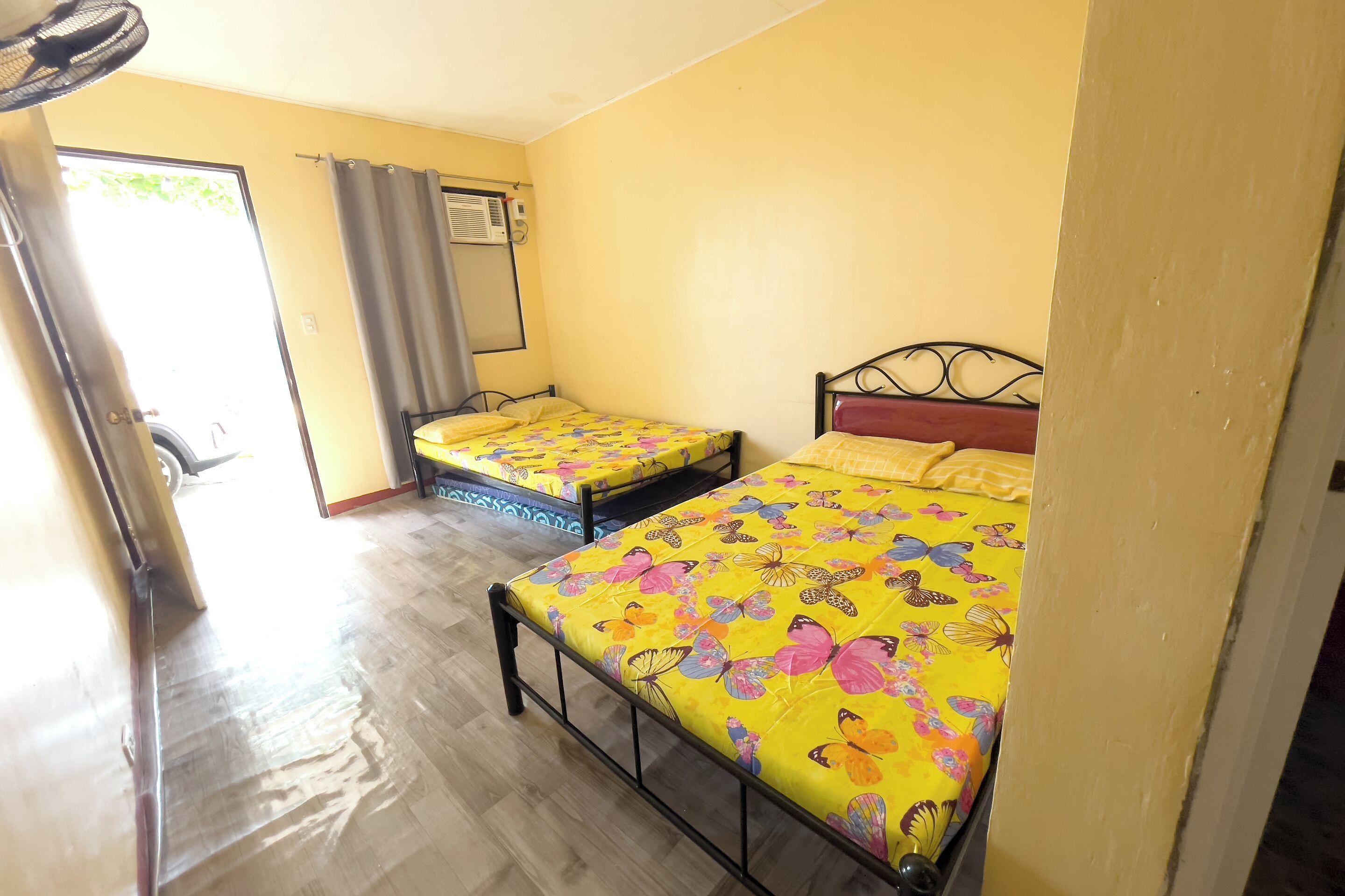 Una camera con due letti, ognuno con una coperta a fiori, una ventola a soffitto e un condizionatore d'aria.