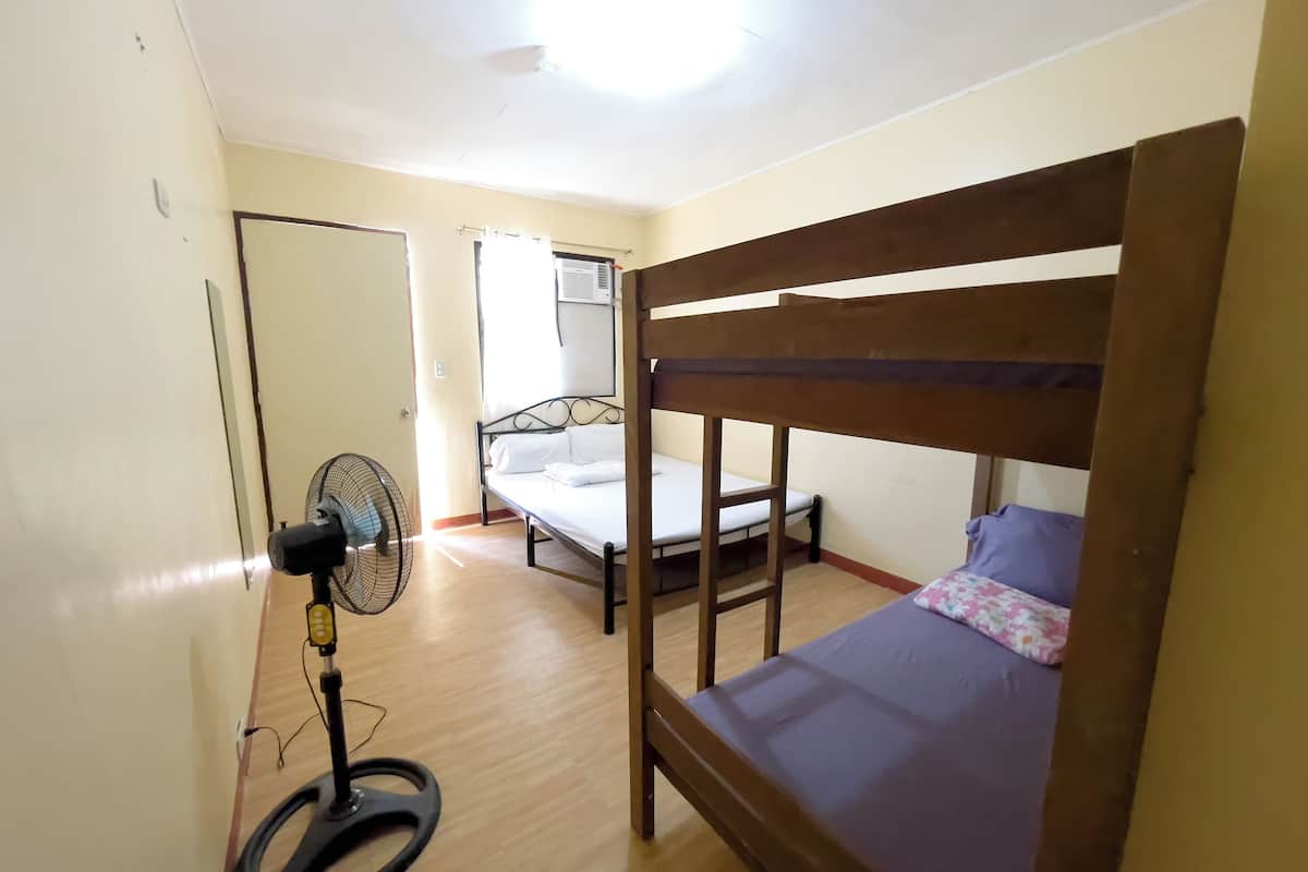 A dormitory room with bunk beds, a standing fan, and an air conditioning unit.