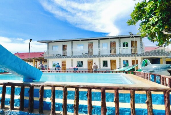 A swimming pool with a wooden deck, a building with multiple rooms in the background, and a clear blue sky. - Sea Master Beach Resort (Lian)