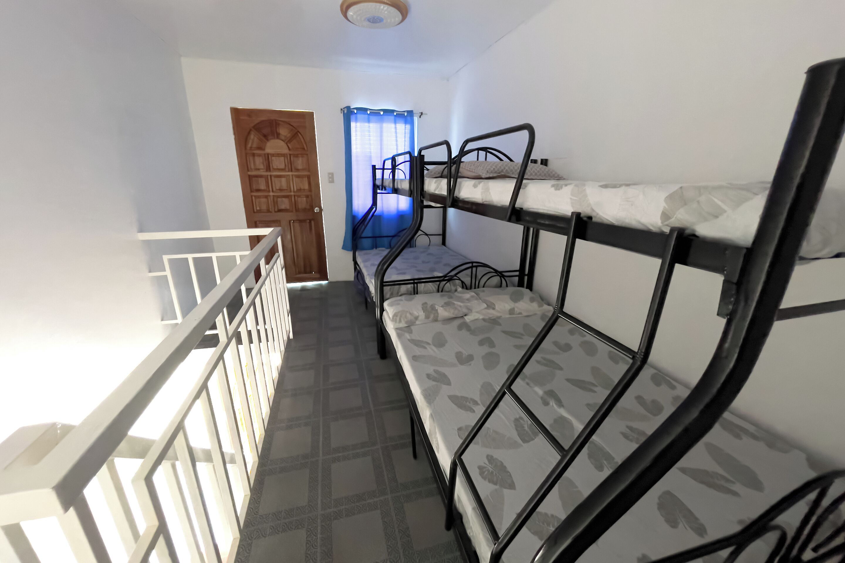 A room with bunk beds, a wooden door, and a window with blue curtains.
