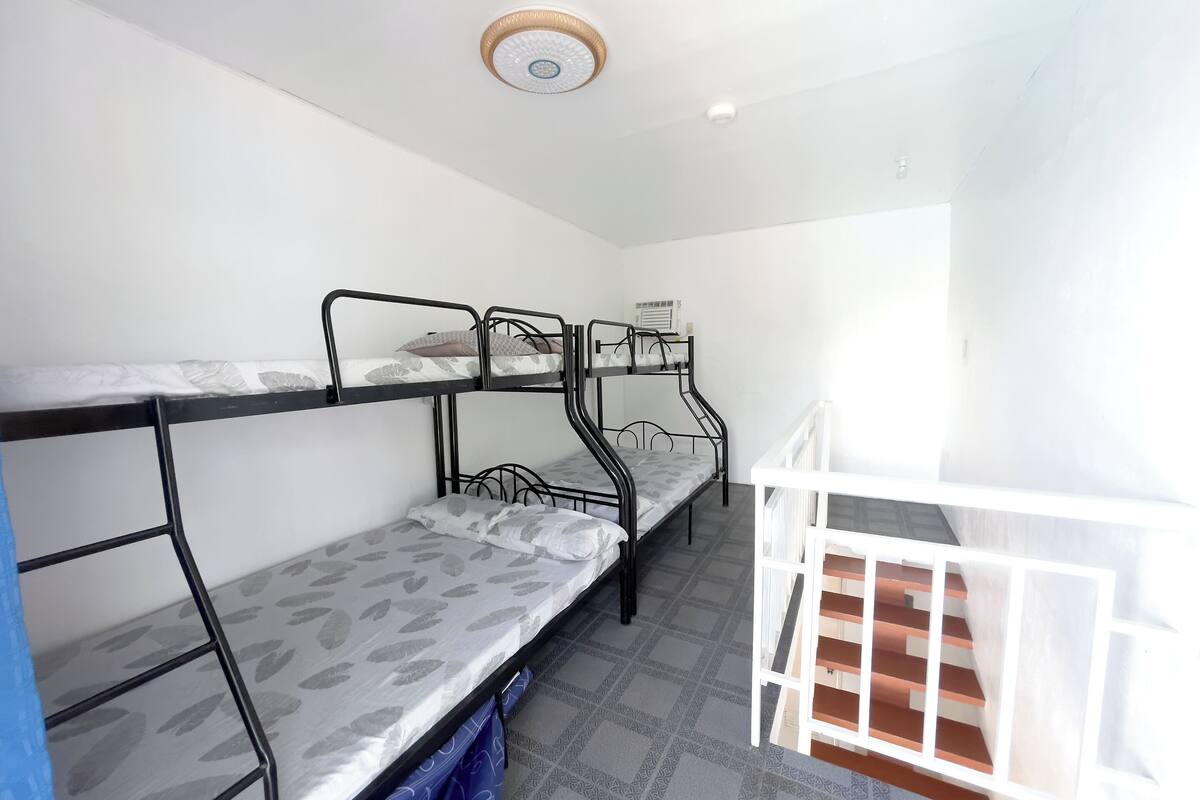 A dormitory room with bunk beds, a white crib, and a small heater on the wall.
