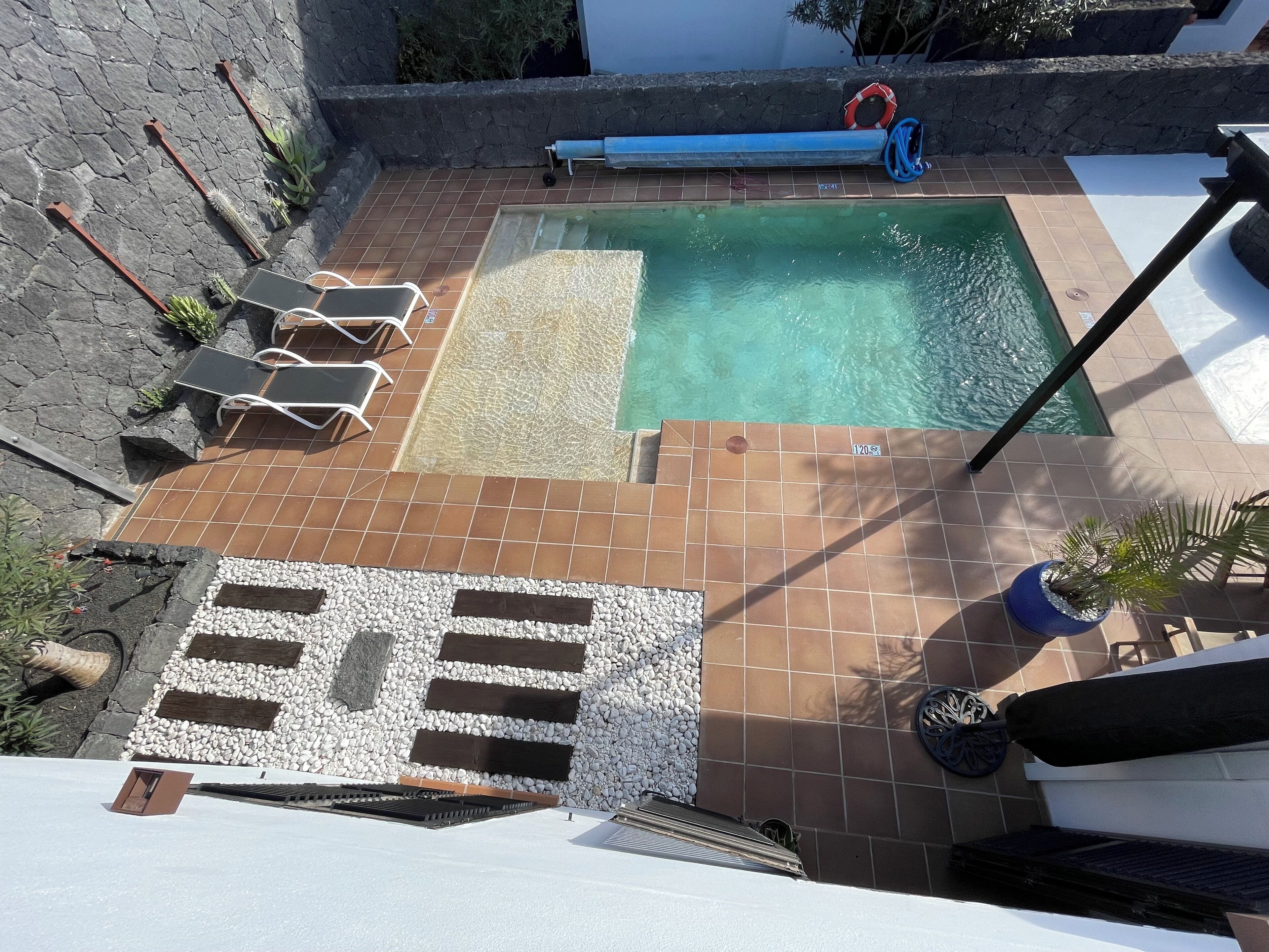 En pool på taket med ett litet bubbelbad, omgiven av solstolar och krukväxter.