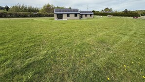 A modern building with a flat roof and solar panels, surrounded by a large grassy field with scattered yellow flowers.