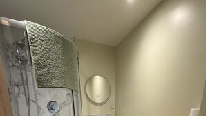 A modern bathroom with a glass-enclosed shower, a white toilet, a vanity with a mirror, and a marble backsplash.