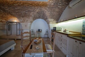A cozy room with a stone ceiling, a dining table with chairs, a bed, and a kitchenette.
