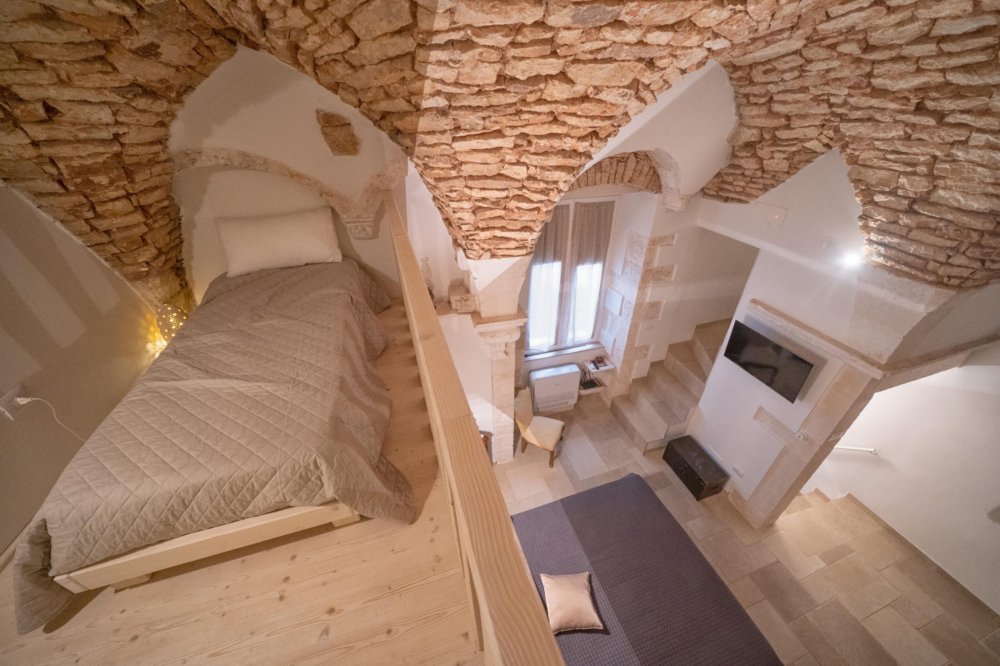 Un dormitorio con techo de piedra, una cama, un escritorio pequeño y una ventana.