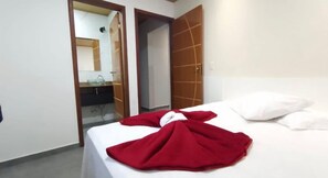 A hotel room with a bed, a red blanket, white pillows, a mirror, and a bathroom visible through an open door.