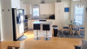 A modern kitchen with white cabinets, a stainless steel refrigerator, a built-in oven, and a coffee maker. There is a dining area with a round table and four chairs. - Spacious 3 Bed/2 Bath, Sleeps 8 in Ocean Lakes!! (Myrtle Beach)