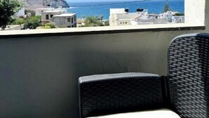 A balcony with wicker furniture, overlooking a coastal view with buildings and a mountain.