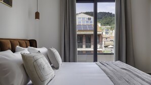 Ein Hotelzimmer mit einem großen Bett, grauen Vorhängen, Blick auf Gebäude und Grünflächen sowie einer hängenden Pendelleuchte.