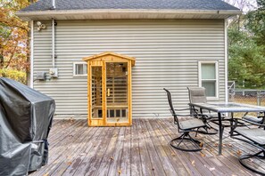 A covered patio with a wooden pergola, a table and chairs, and a grill. - Lake George Getaway: Cozy cottage w/ kayaks, cornhole, Xbox, volleyball (Harrison)