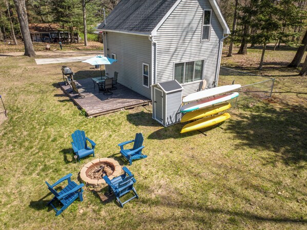 A house with a deck, outdoor seating, a fire pit, and canoes. - Lake George Getaway: Cozy cottage w/ kayaks, cornhole, Xbox, volleyball (Harrison)