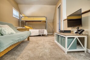 A compact room with bunk beds, a sofa, a desk with a flat-screen TV, and storage cabinets. - Lake George Getaway: Cozy cottage w/ kayaks, cornhole, Xbox, volleyball (Harrison)