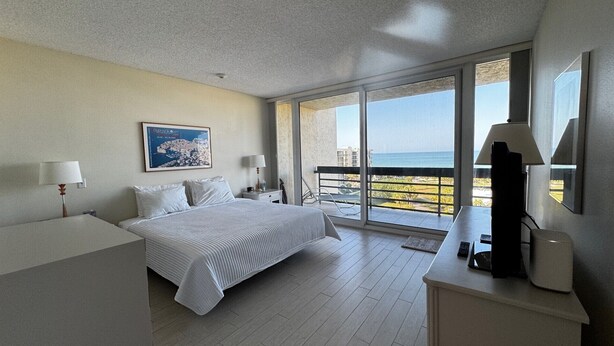 A hotel room with a bed, a desk, a chair, a TV, a balcony with a view of the sea, and a framed picture on the wall. - Charming 2-bedroom condo with AC, fitness room in wonderful Longboat Key (Longboat Key)