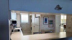 A modern kitchen with a central island, a built-in oven, and a refrigerator. There are two framed posters on the wall and a window with blinds. - Charming 2-bedroom condo with AC, fitness room in wonderful Longboat Key (Longboat Key)