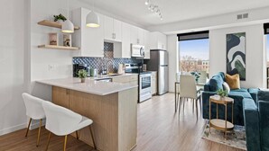 Una cocina moderna con armarios blancos, una isla central y una zona de comedor con un sofá azul y una mesita auxiliar.
