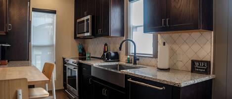 A modern kitchen with dark wood cabinets, a granite countertop, a built-in microwave, a stainless steel sink, and a window providing natural light.