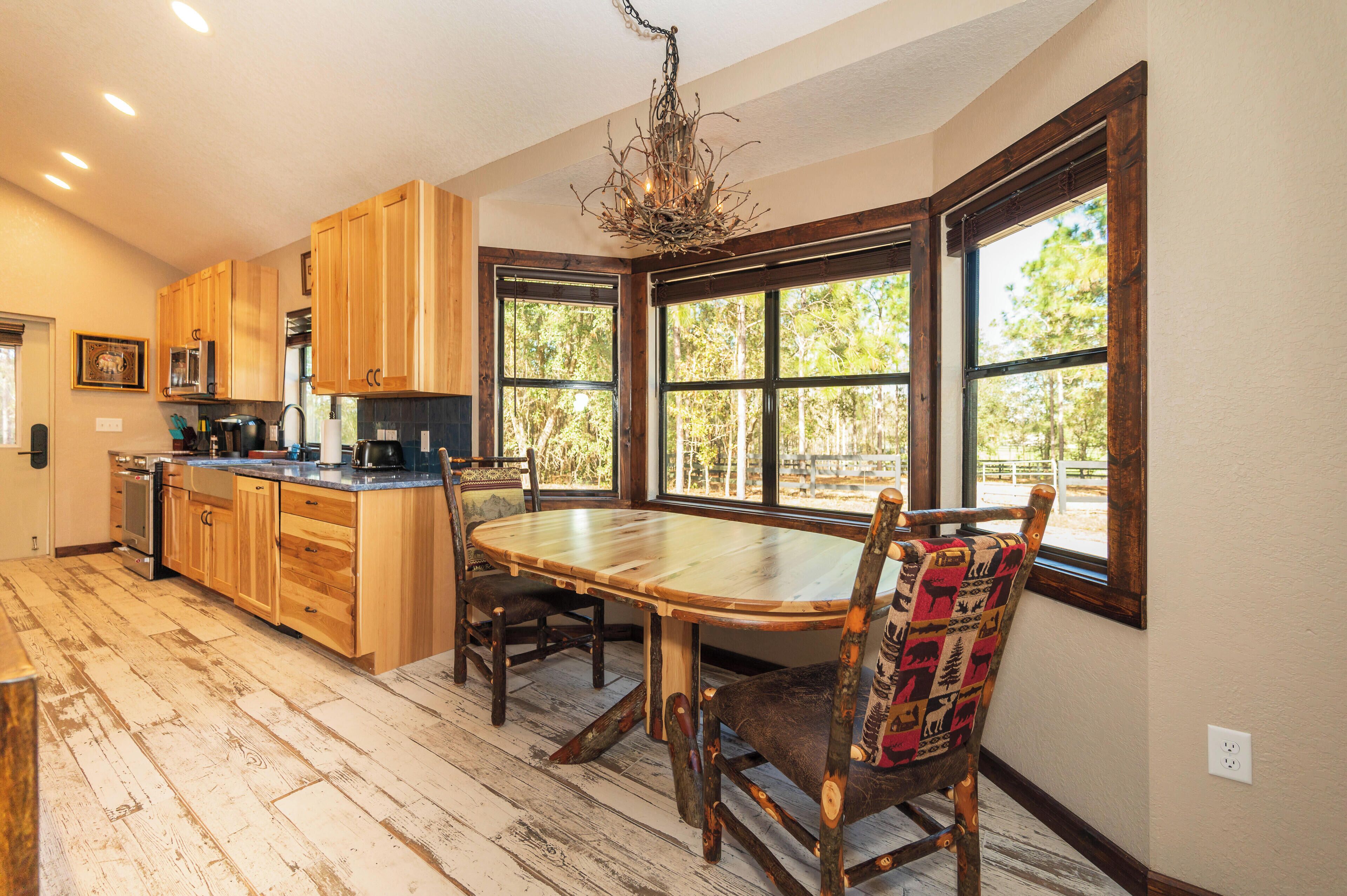A kitchen with wooden cabinets, a dining table, and large windows.