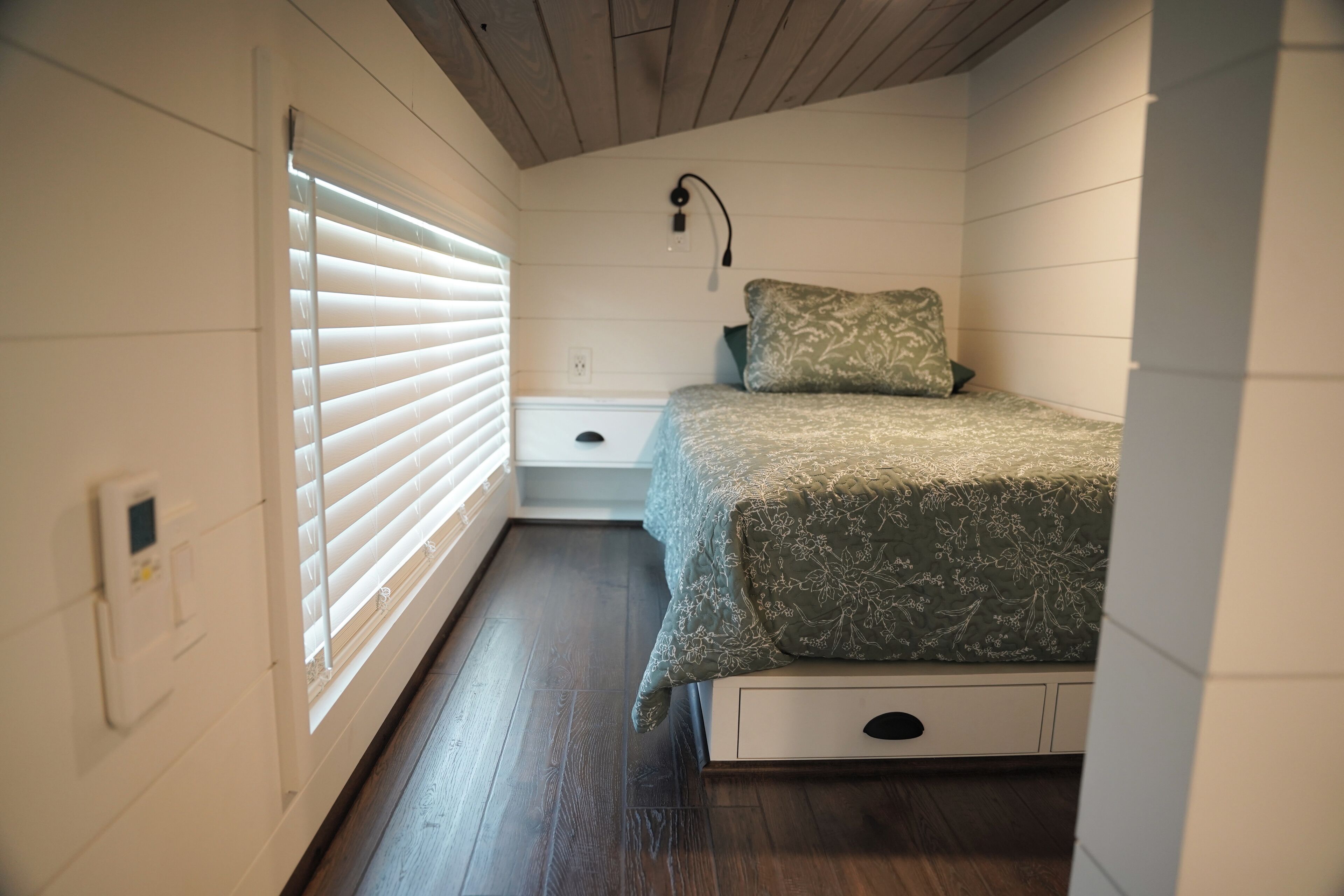 Une chambre à coucher comprenant un lit, une table de chevet, une lampe fixée au mur et un thermostat.