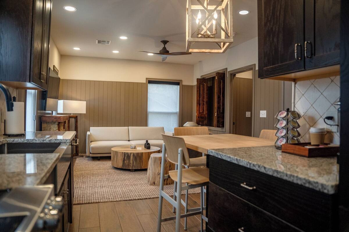 A modern kitchen with dark cabinetry, a central island, and a dining area with a sofa and chairs.