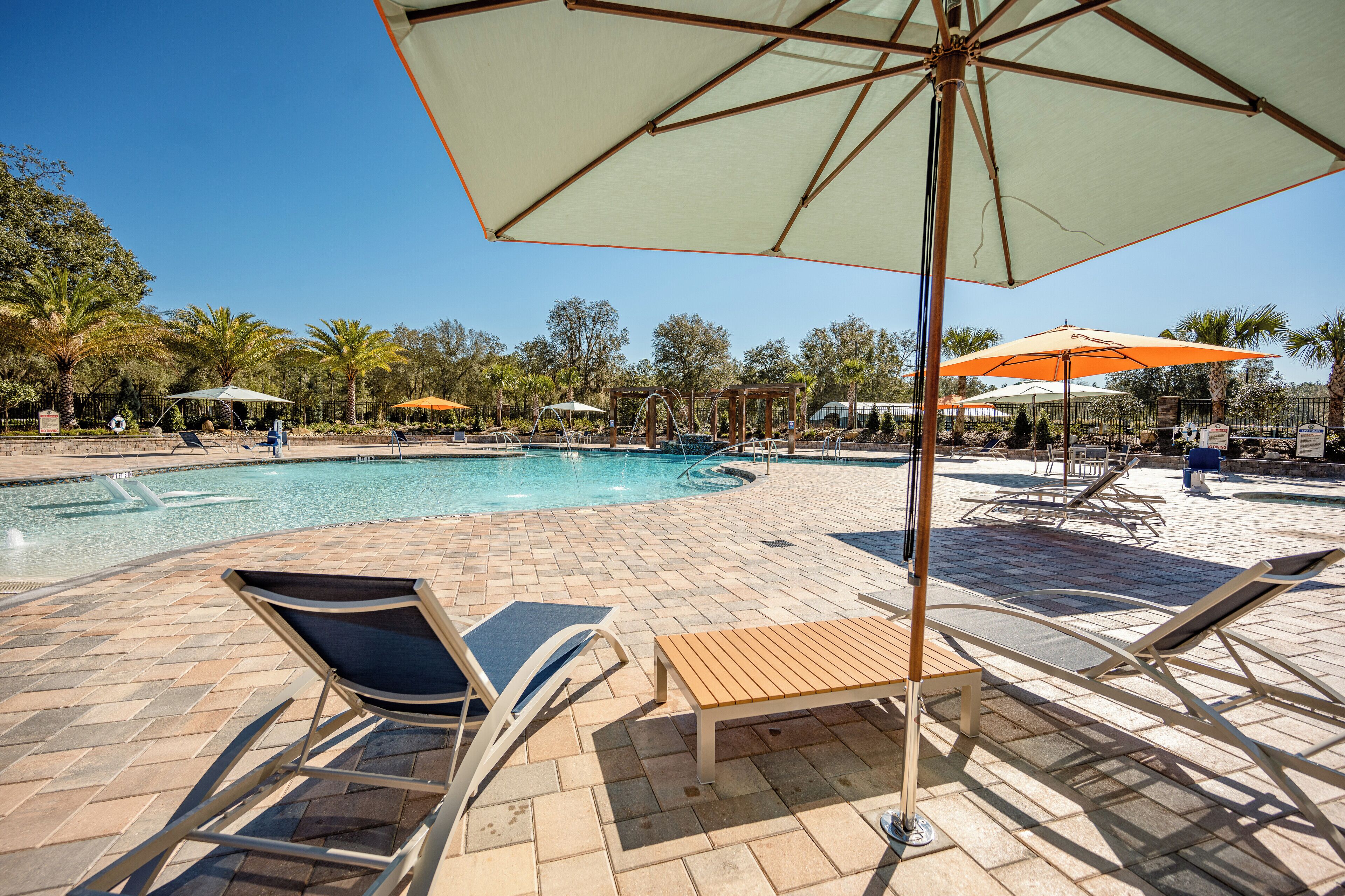 A pool area with lounge chairs, umbrellas, and a wooden bench.