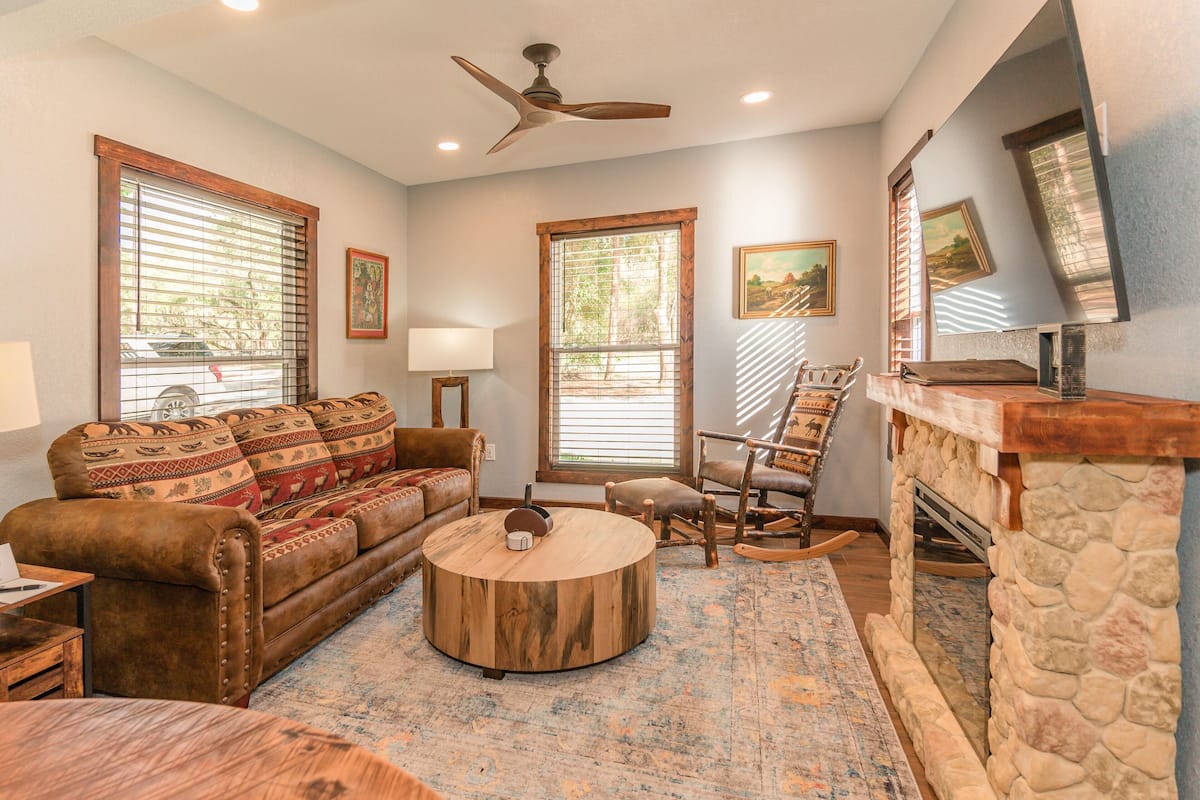 A living room with a brown leather sofa, a round coffee table, a wooden rocking chair, and a stone fireplace.
