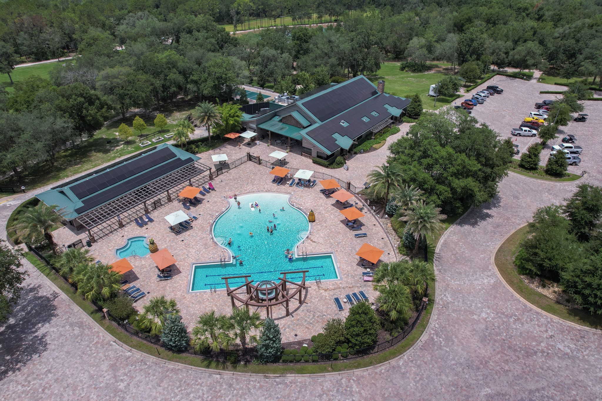 An aerial view of a resort with a central swimming pool, sun loungers, and a covered outdoor area.