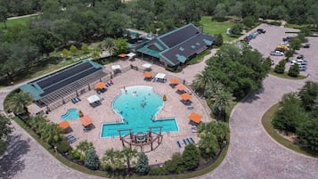 An aerial view of a resort with a central swimming pool, sun loungers, and a covered outdoor area.