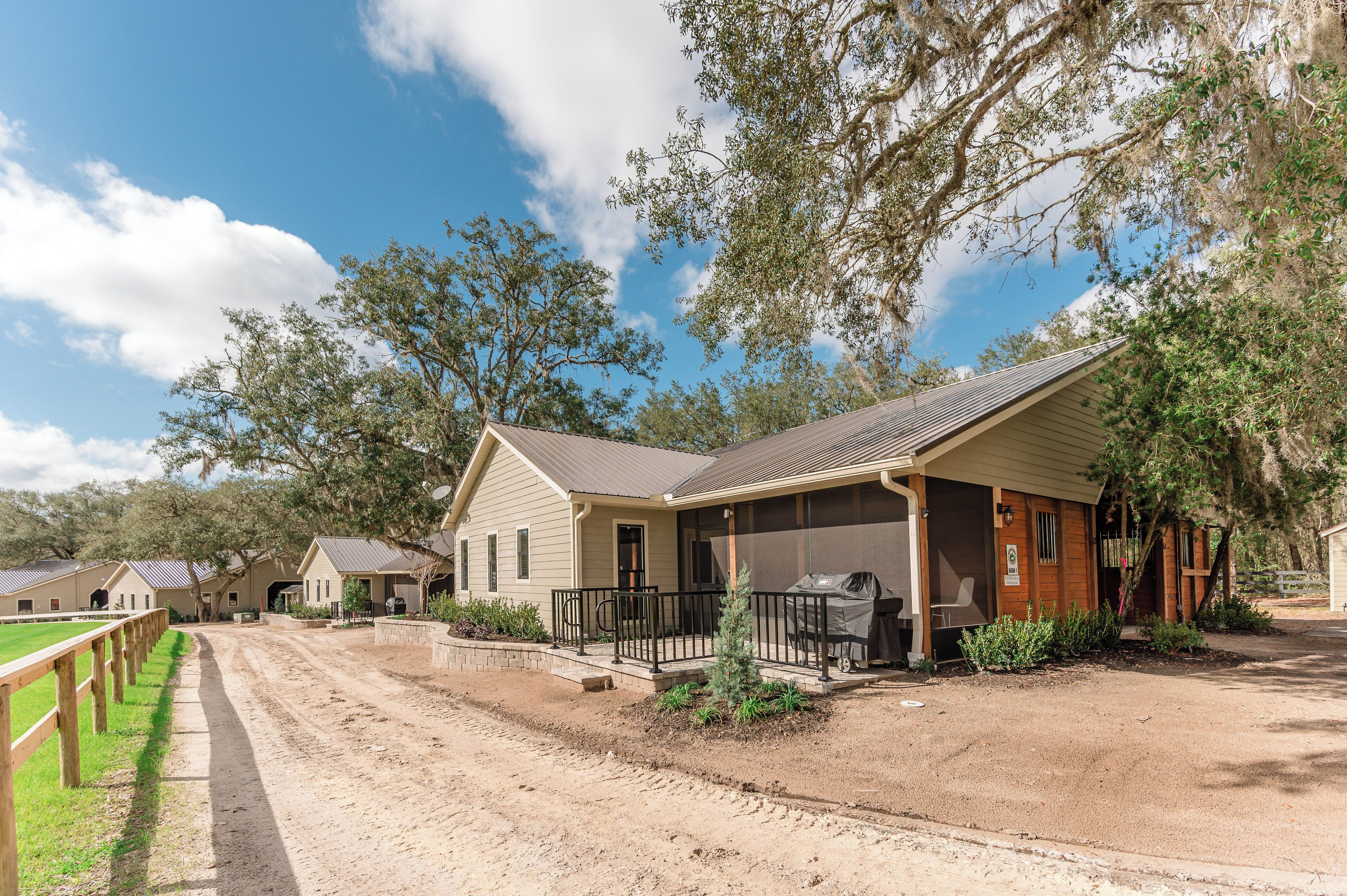 A ranch-style building with a porch, a covered outdoor seating area, and a fenced-in horse riding area.