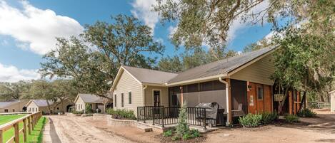 A ranch-style building with a porch, a covered outdoor seating area, and a fenced-in horse riding area.