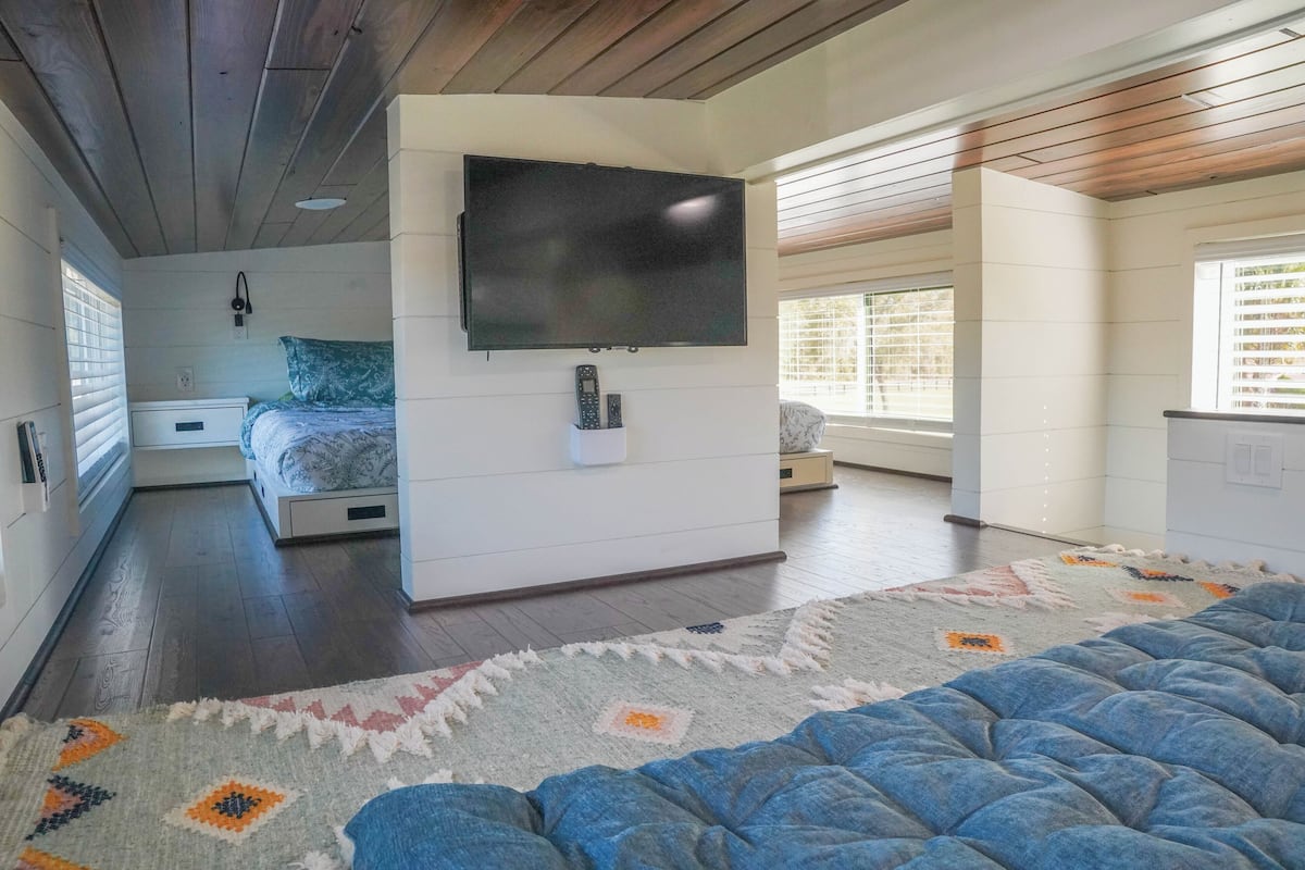 A modern bedroom with a large bed, a flat-screen TV mounted on the wall, and a cozy rug.