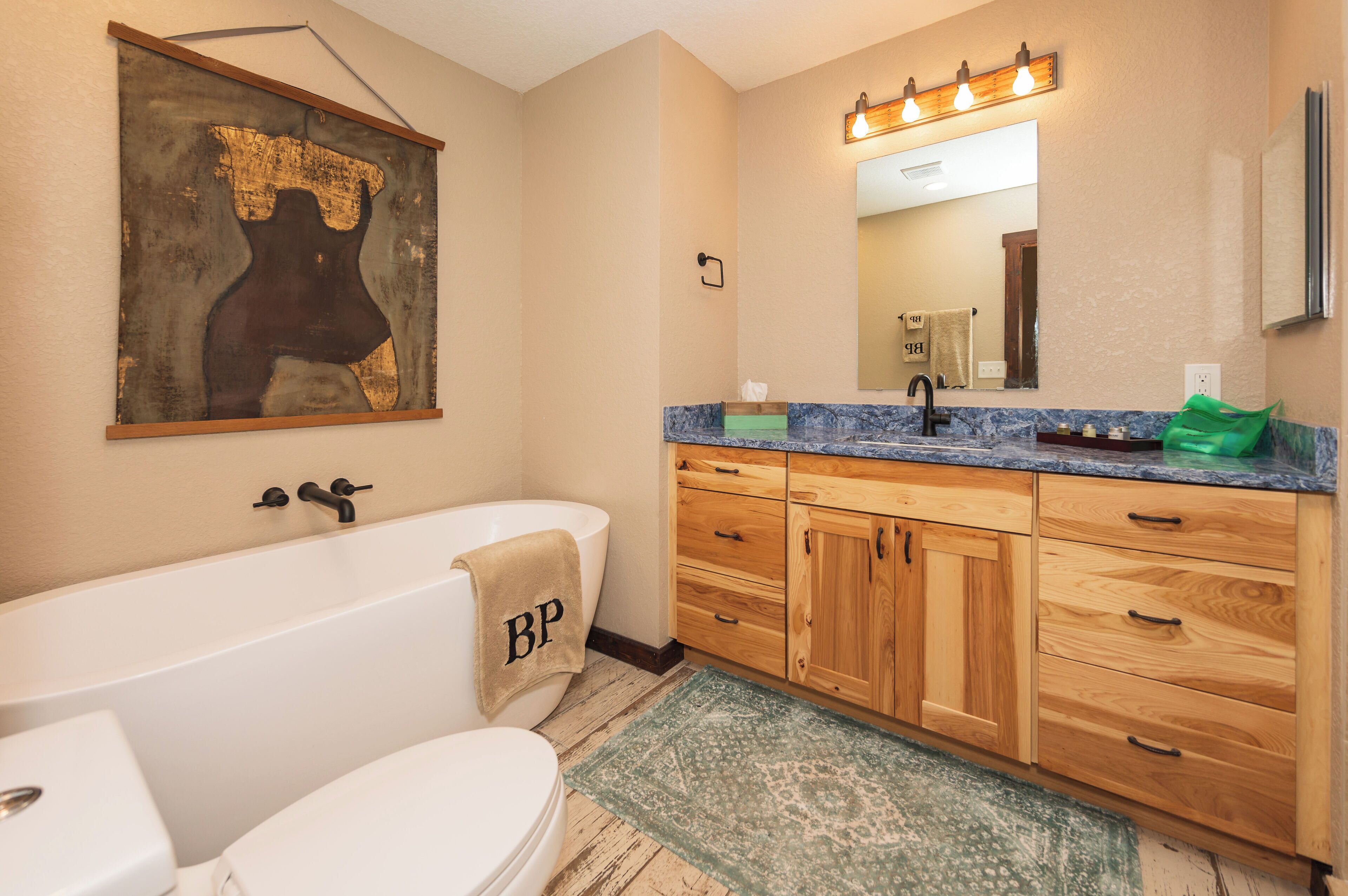 Une salle de bain avec une baignoire, des toilettes, des meubles en bois, un lavabo avec un miroir et une serviette ornée des lettres « BP ».