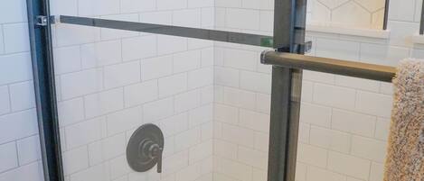 A glass-enclosed shower with white tiled walls and a glass door.