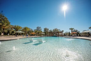 A clear blue pool with lounge chairs and umbrellas, surrounded by palm trees and a pergola. - Black Prong Resort (Bronson)