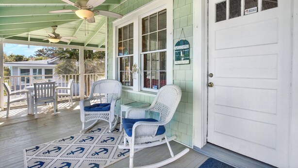 A porch with rocking chairs, a table, and a ceiling fan.