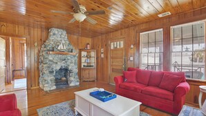 A wooden interior with a stone fireplace, red sofa, and a ceiling fan.